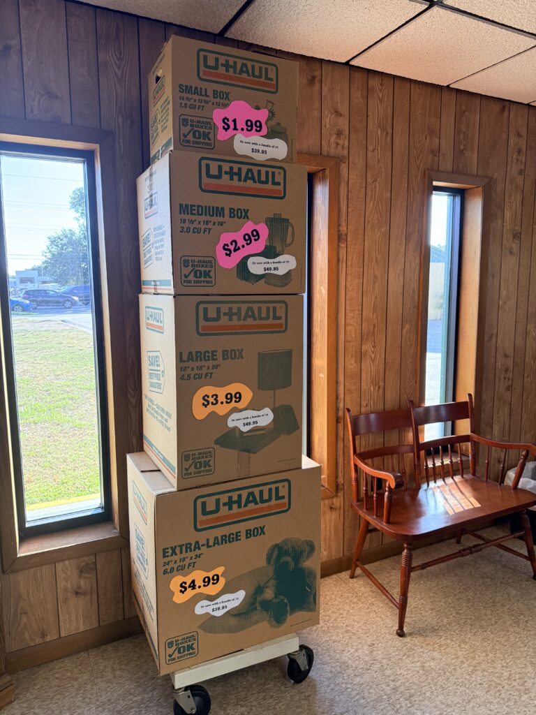 Stacked U-Haul moving boxes in a corner of a room, labeled with prices: small ($1.99), medium ($2.99), large ($3.99), and extra-large ($4.99).