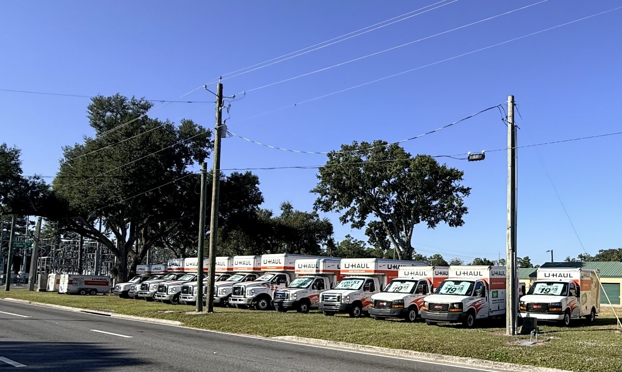 Row of U-Haul rental trucks parked along a roadside, showcasing rental prices. The setting indicates a vehicle rental service for moving needs.